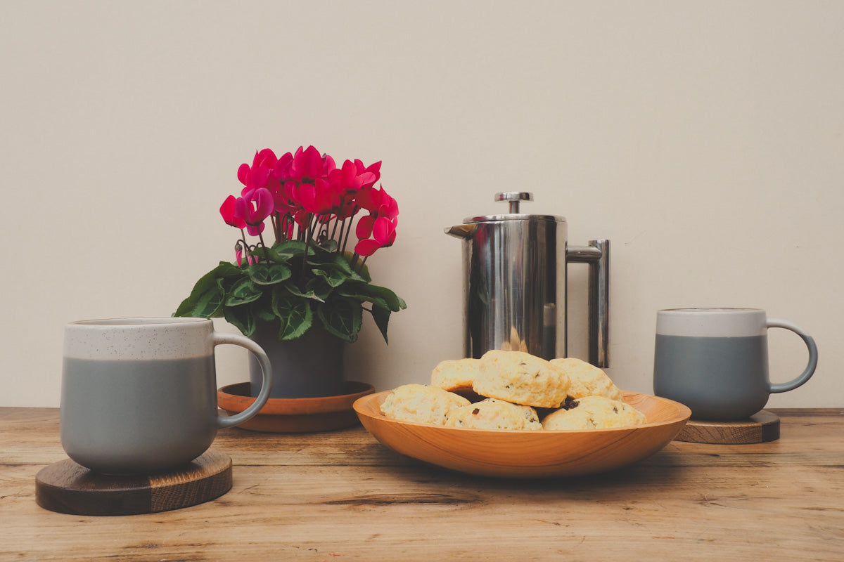Handcrafted wooden coasters in use with pile of scones in a wooden bowl.